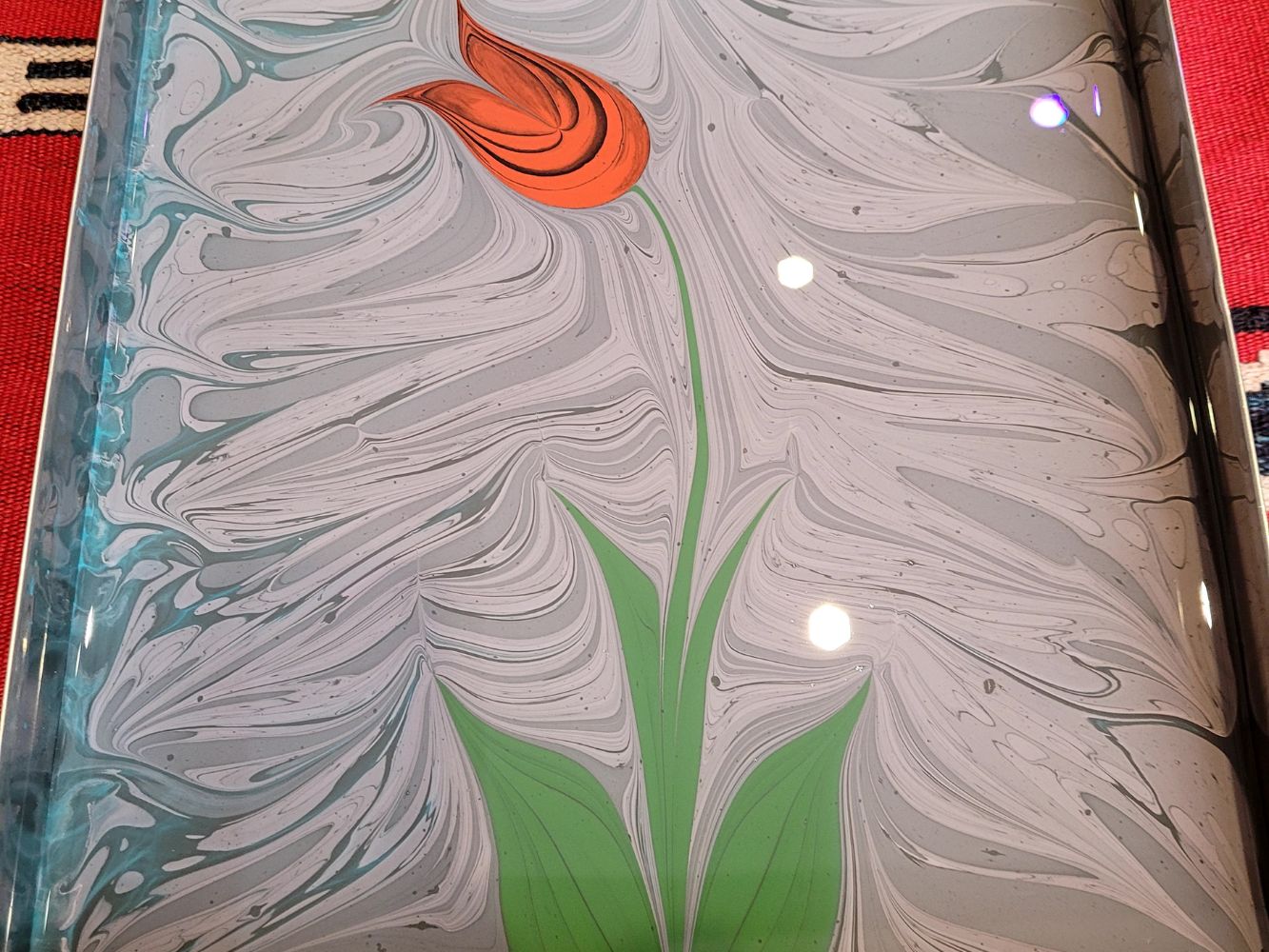 Completed ebru (Turkish water marbling) paper featuring a red tulip and green stems